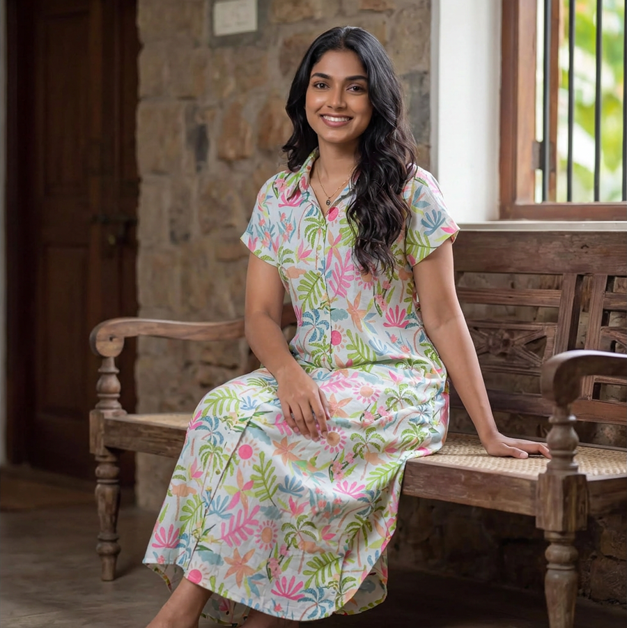 Woman sitting on a wooden bench wearing a colorful tropical print summer dress with a collar.